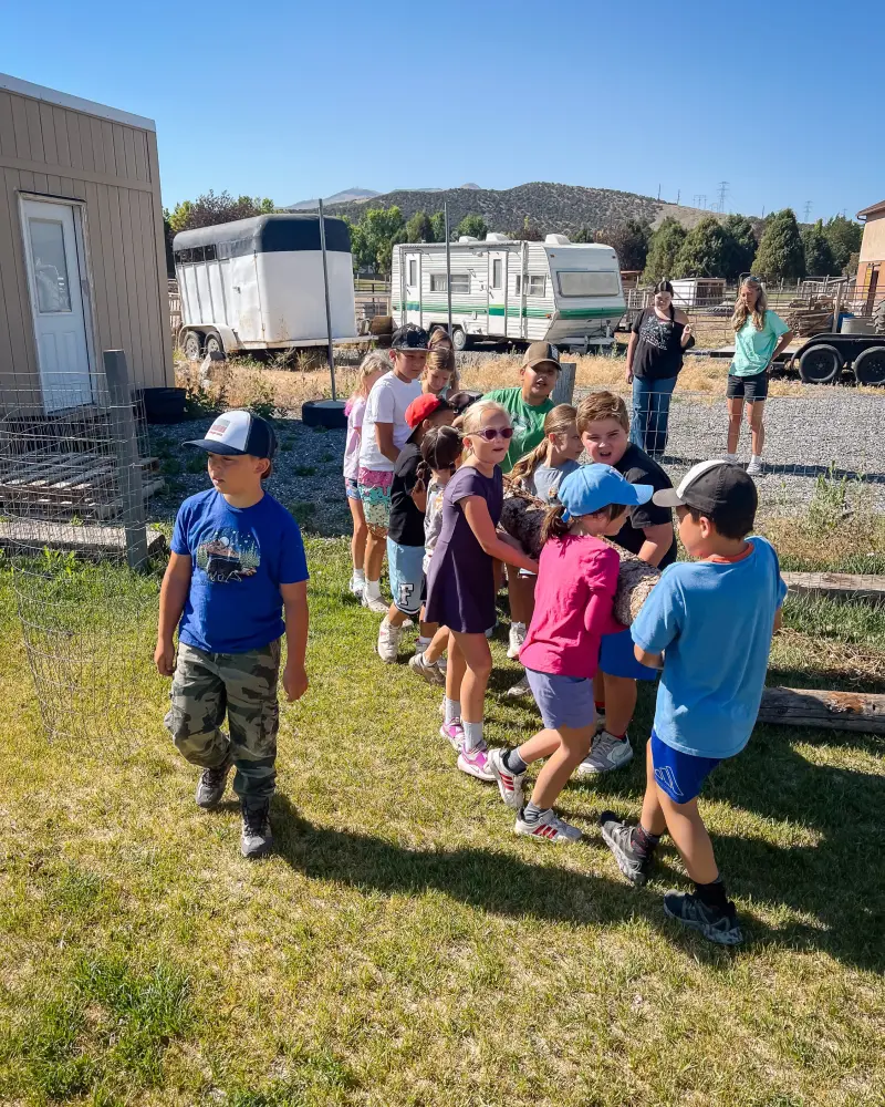 A line of campers carrying a log together across the grass