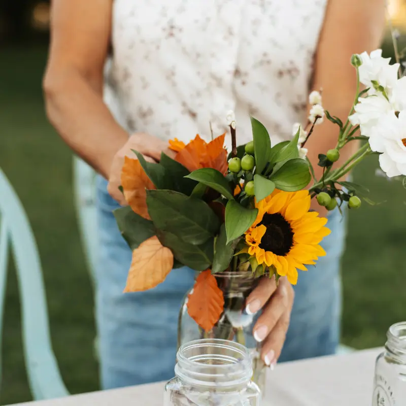 Setting a jar of sunflowers, white blooms and autumn leaves on the table