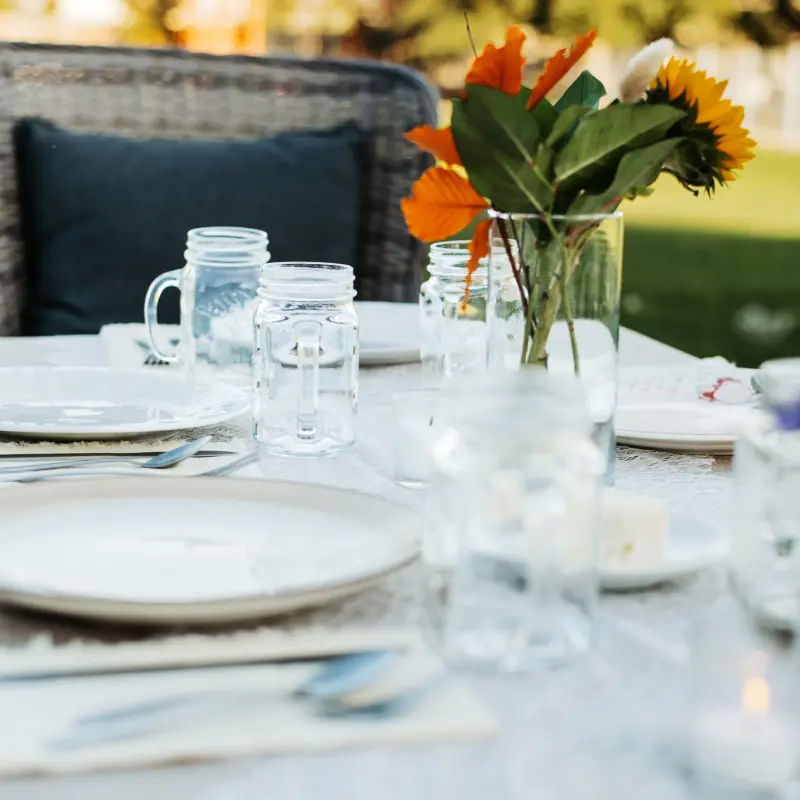 A place setting with mason jar mugs and a jar of sunflowers and orange leaves, the lawn beyond