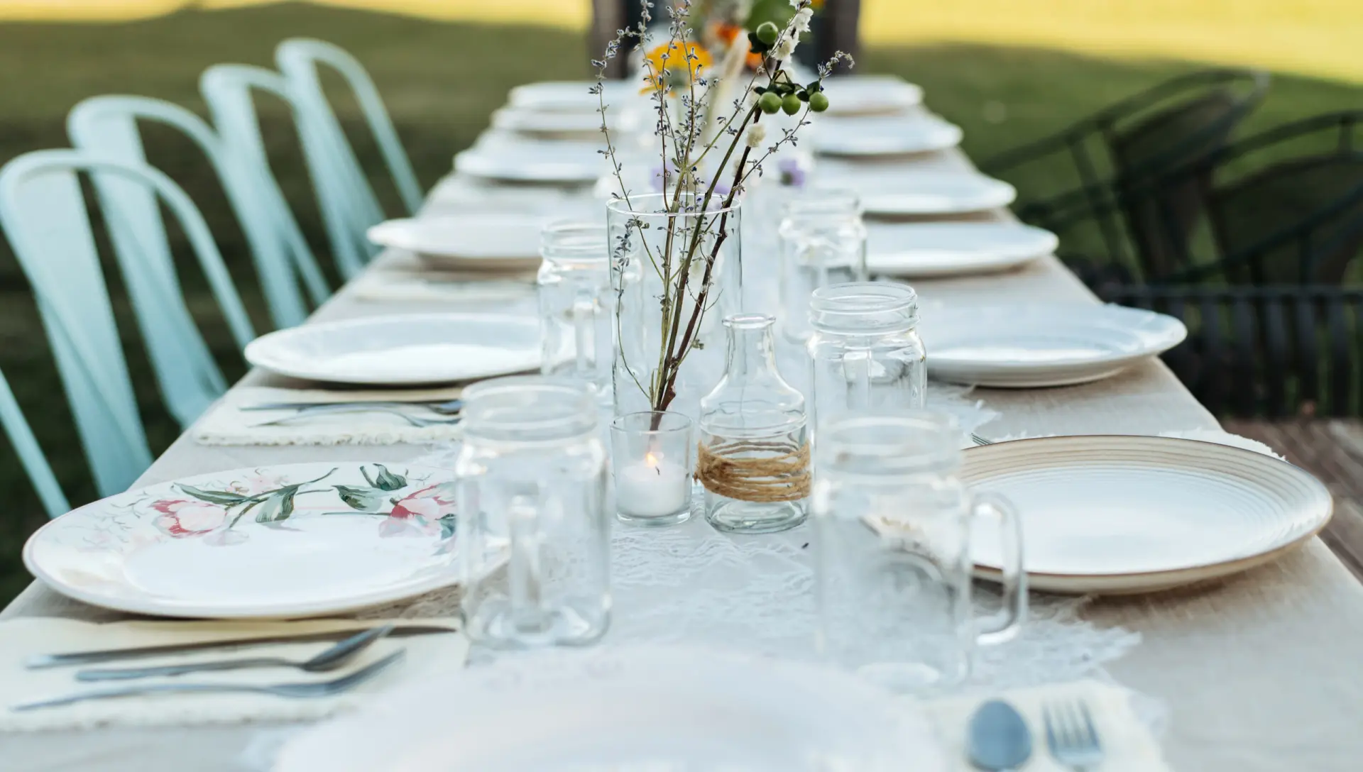 A long table set with white plates, mason jars, candles and wildflowers in glass bottles