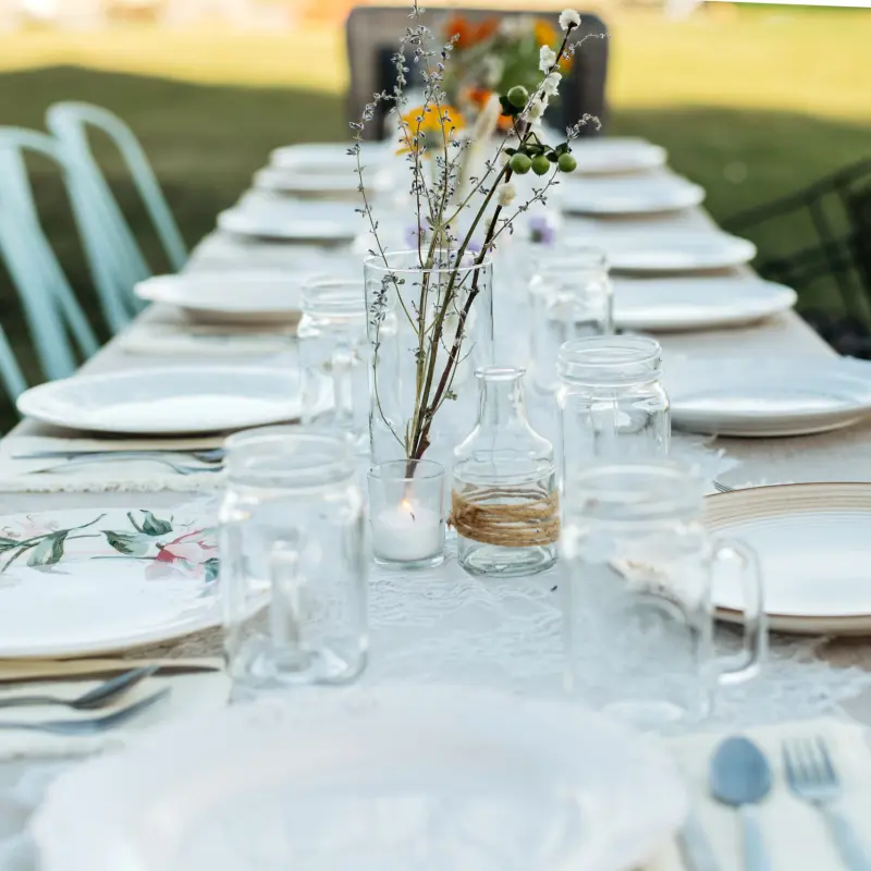 A long table set with white plates, mason jars, candles and wildflowers in glass bottles